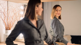 Self-confident Woman looking at her reflection into the mirror indoors. Beautiful interior design